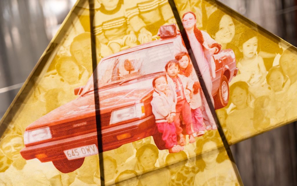 Christine Ko and Louis Kim, 'Departure' exhibition to show at Museum of Brisbane. Photo: Louis Lim. A kite with a background made from a family photo in yellow hues, in the foreground in red is a mother with young children standing in from of a vintage car.