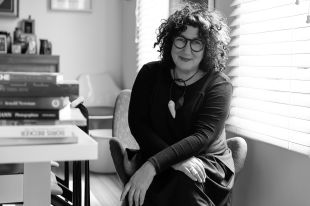 Black and white photo of a woman with curly hair and glasses wearing a black dress. Stella Day Out.
