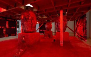 Candice Lin, ‘Lithium Sex Demons in the Factory’, 2023. Photo: Izzy Leung. A spaced washed in red lights with large-scale oval vessels standing on rustic platforms. It appears to be underground, with a foreboding ambience. To be shown at MUMA.