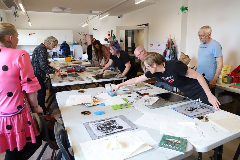 A group of people working on drawing in a casual environment. They are standing and reaching across the table for different material. 