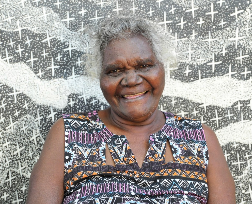 Aboriginal woman with her art in background.