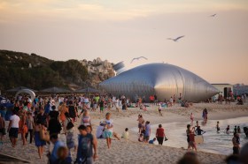 Anniversaries. Sculpture of big silver pillow on crowded beach.