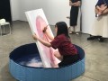 Artist Sayoko Suwabe in a small blue paddling pool scraping off the paint on one of her portraits. Uncertain Contours of Images. Sayoko Suwabe.
