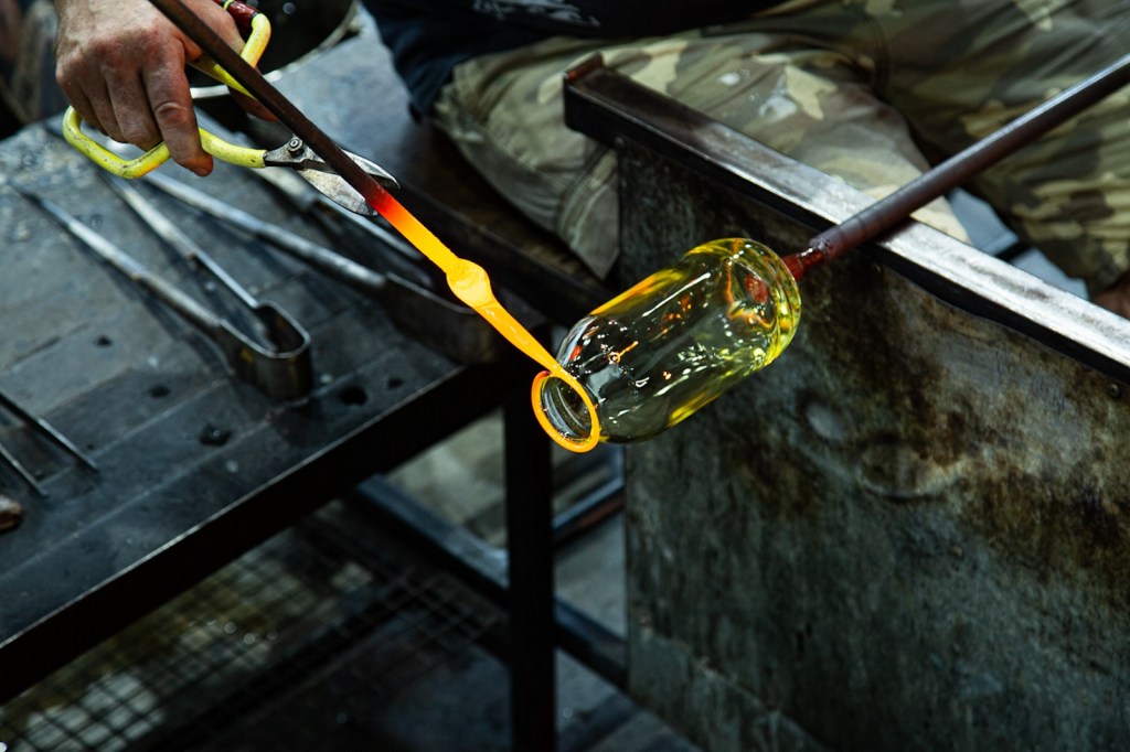 Glass blowers bench with artist reforming a bottle. Small Impact Studio.