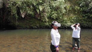 UQ Art Museum. Image is two people wearing white shirts standing in a river with VR headsets on.