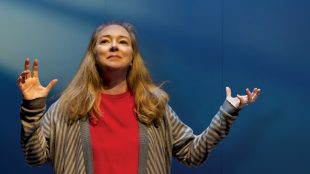 Tiny Beautiful Things. Image is a middle-aged woman in a red shirt and brown cardigan, with long fair hair. She is holding her hands up in the air with her elbows bent, as if explaining something.