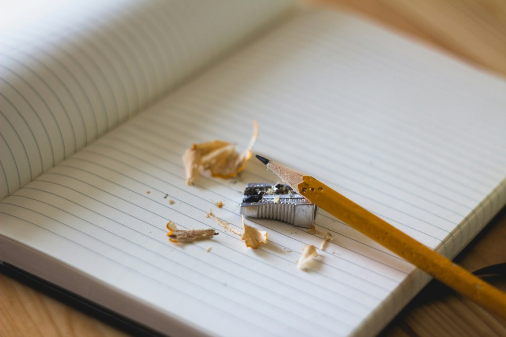 Literary journal. A freshly sharpened pencil sits amid pencils shavings and a pencil sharpener on a blank page, suggesting the start of a new creative writing project.
