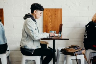 young person with hoodie working on laptop in a cafe. Freelancer.