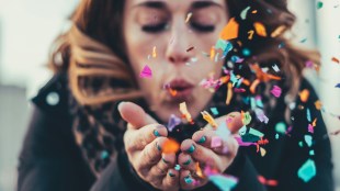 Woman blowing confetti out of hands. Arts news.