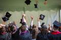 University students in graduation robes throw mortarboards in the air.