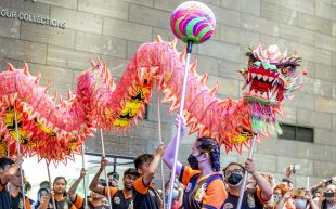 Dragon dances at the NGV Lunar New Year Celebrations, taking place from 10 – 11 February at NGV International, Melbourne. Photo: Eugene Hyland. A peachy pink dragon puppet is held by dragon dancers inside the concrete walls of NGV’s Great Hall. They are surrounded by a big crowd of visitors.