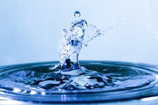 A dramatic close-up of a drop of water falling into a pool of water and the resulting splash and ripples.