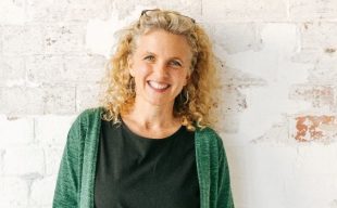 Sally Rippin. Woman with green cardigan over black t-shirt and curly shoulder length blonde hair with glasses on her head smiles at the camera.