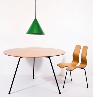 A wooden table, green pendant light and abstract wooden chair in a white room.