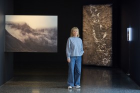 Ellen Dahl stands between two large scale photographs of landscapes.