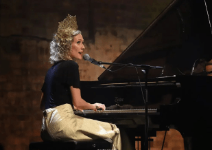 Emma Dean, a Brisbane artist, plays the piano and sings in the microphone. She and other artists compete with international star Taylor Swift.
