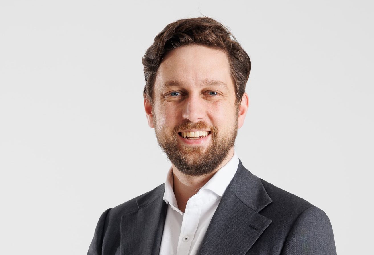 Head shot of Caucasian man with short dark hair and a neat beard, wearing a white open necked shirt and grey suit jacket. Digital Futures.