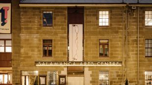 A heritage-listed former warehouse that is now an arts centre. The photo shows the sandstone which makes up the building, several windows, and a sign reading 'Salamanca Arts Centre' above the main entrance.