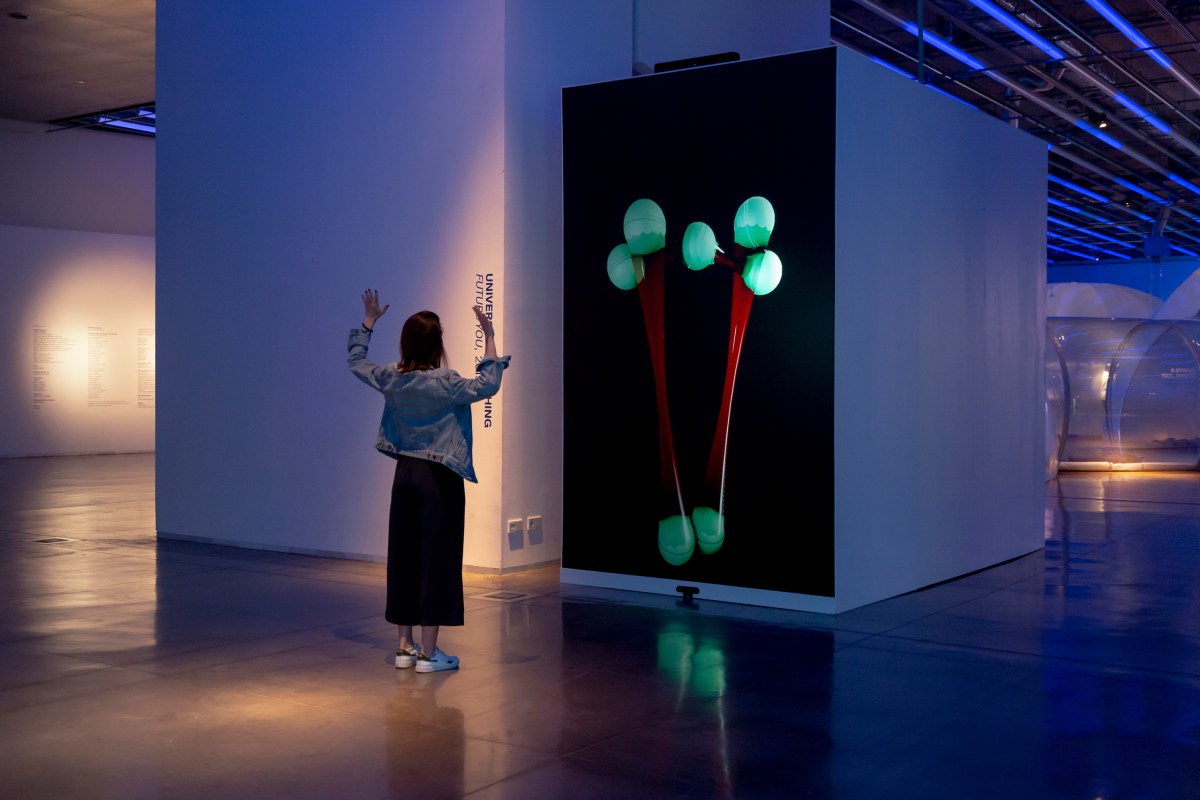 Universal Everything. A woman stands in front of a large screen. On the screen, two tall structures react to her movement.