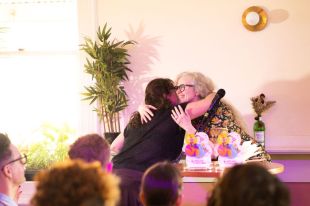 philanthropy: a woman hugging another woman in front a small audience at an awards ceremony.
