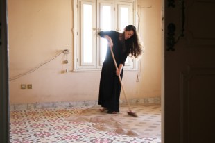 Woman in black dress sweeping up sand artwork in old building