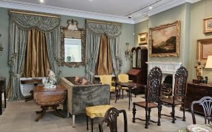‘Fit for a King: Vincent Jenden Reimagines The Johnston Collection’. Photo: ArtsHub. An elaborate lounge room with elegant decor. The walls are painted a light pastel green and artworks are hang across the walls and antique furniture is on display.