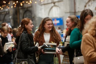 A group of young women are standing outside under strings of lights holding books and talking. Sydney Writers' Festival.