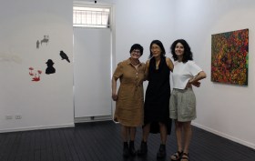 Three female artists stand in front of their artwork in the Woolloongabba Art Gallery.