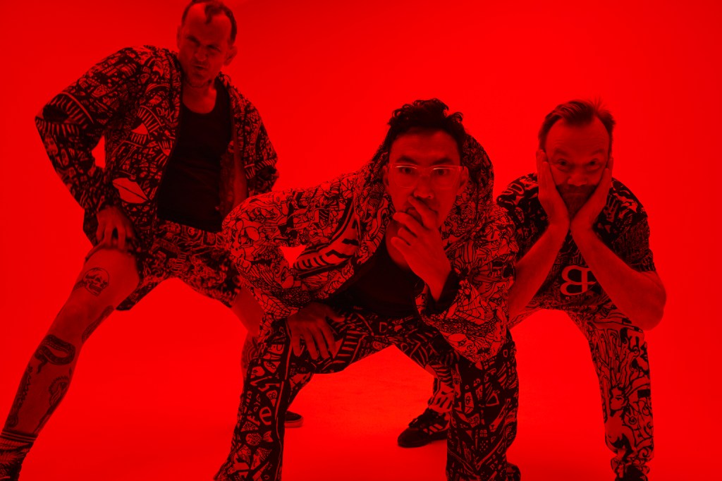Open Season. The image shows three young men in streetwear leaning forward towards the camera, holding their chins thoughtfully, against a bright red background.