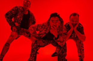 Open Season. The image shows three young men in streetwear leaning forward towards the camera, holding their chins thoughtfully, against a bright red background.