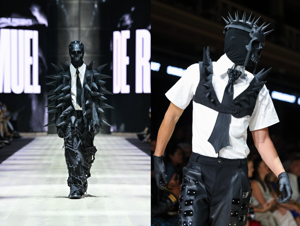 Designs by Samuel de Raadt at the Paypal Melbourne Fashion Festival 2024 National Graduate Showcase. Photo: Lucas Dawson. Two models are shown on the runway. On the left is a model wearing a skull mask completely covering their face, a black suit with spikes, a white shirt with a black tie and long black pants with frayed cutout holes. On the right is a model also wearing a black skull mask with spikes on their head, a white shirt with black tie and a cropped black vest with spikes. The pants are paneled with leather and small black embellishments.