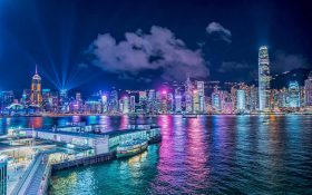 Photo: Daniam Chou, Unsplash. Hong Kong cityscape at night with brightly lit skyscrapers seen across the harbour.