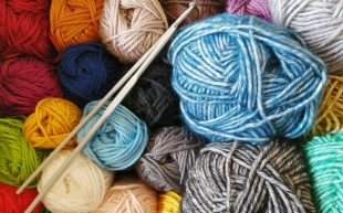 Photo: Margarida Afonso, Unsplash. Spools of colourful yarn stacked together with a pair of knitting needles.