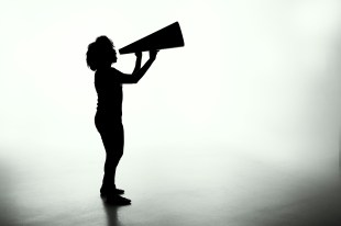 A striking black and white photograph of a woman holding a megaphone; she is completely silhouetted against the white background.