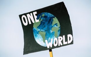 Photo: Markus Spiske, Pexel. Protest poster with black ground, image of the earth, and the text 'ONE WORLD'.