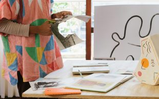 Photo: RF._.studio, Pexels. Hands cutting out design drawings for project in a light-filled studio space. There are books and reference images on a wooden table.