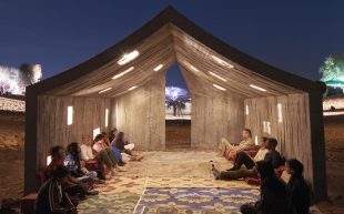 DAAR’s Concrete Tent for the Sharjah Architecture Triennial 2023, curated by Tosin, who will be delivering a keynote for Melbourne Design Week 2024. Photo: Edmund Sumner. A large tent structure in a desert environment at night with people sitting on tapestry , hanging out.