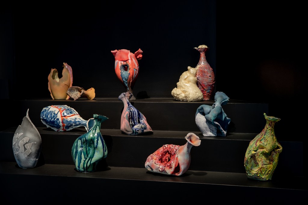 Timothy Yap, ‘The beauty in chaos’, 2023, installation view at ‘Top Arts 2024’. Photo: Kate Shanasy. Broken and seemingly “failed” ceramics, featuring 10 vessels each different to the other in form and colour, against a black background. 