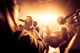 A dynamic photo of a jazz band, taking from behind the trumpet players looking towards the stage lights.