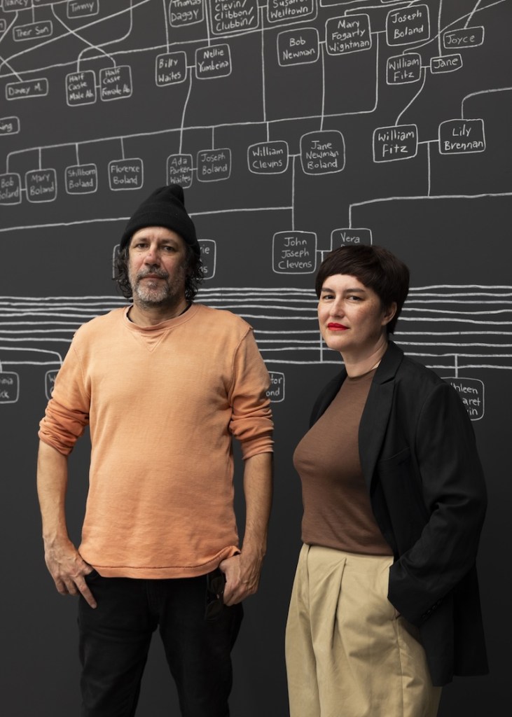 Man with orange shirt and hat and women in art installation with chalk on walls.