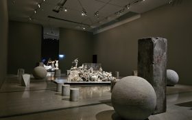 'Nina Sanadze', installation view at The Ian Potter Centre: NGV Australia'. Photo: ArtsHub. In a gallery space with grey walls and tiled floors there are several large installations, including anti-terror barriers that appear like concrete spheres and rectangular blocks, scatters of monuments and sculptures.