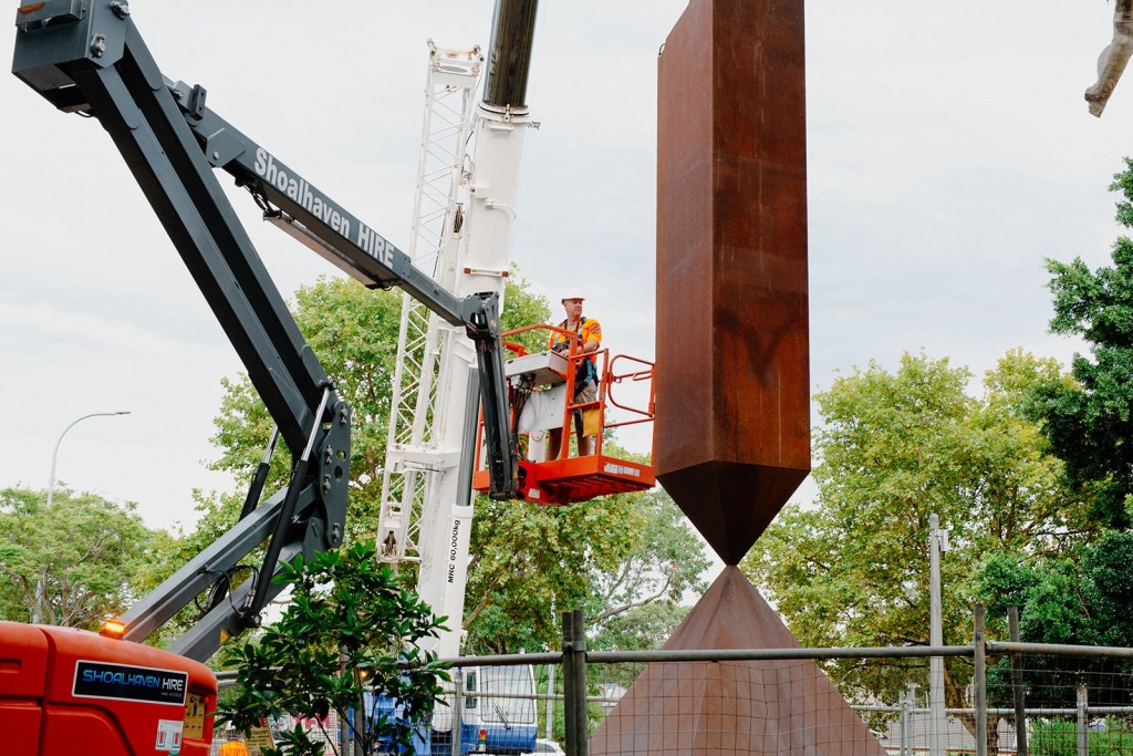Crane operator lifting metal sculpture into place.