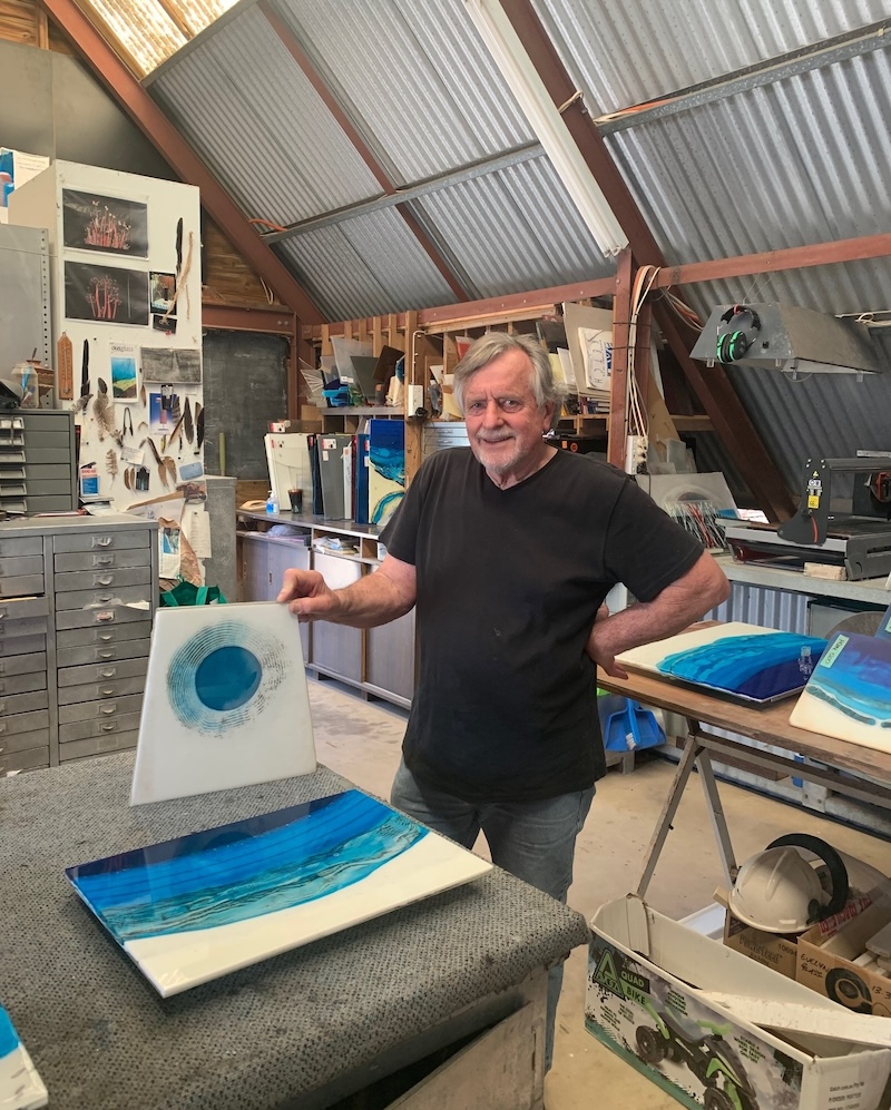 male artist in black shirt in glass studio looking at artworks. Gerry King.