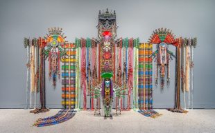 Taipei Dangdai, Evoke sector. Anne Samat, ‘Never Walk In Anyone's Shadow,’ 2023, Rattan sticks, kitchen and garden utensils, beads, ceramic, metal and plastic ornaments. Photo: Brian Holcombe. Image: Courtesy of the artist and MARC STRAUS. A large colourful installation that appears like a folk monument against a grey background.