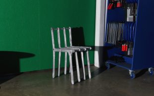 Chair by Andrew Carvolth, who will be showing works as part of Craft Victoria’s Conscious Craft initiative. Photo: Supplied. A aluminium chair constructed out of seperate aluminium bars. It is placed against a green background next to a blue tool rack and lit brightly.
