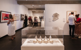 2022 JADA Exhibition at Grafton Regional Gallery. Photo: Melting Wax Photography. People inside a gallery space with white walls and grey floor. Different works of varying scales are hung, while closest to the viewer is a paper-based work enclosed in a glass display.