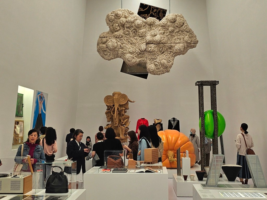 ‘LOEWE Crafted World’, installation view at Shanghai Exhibition Centre. Photo: ArtsHub. A small crowd inside a white exhibition space with high ceilings, showing sculptures, alongside handbags, and other design material.