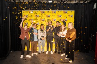 A group of comedians stand in front of a melbourne International Comedy Festival poster with ticker tape flying all around.