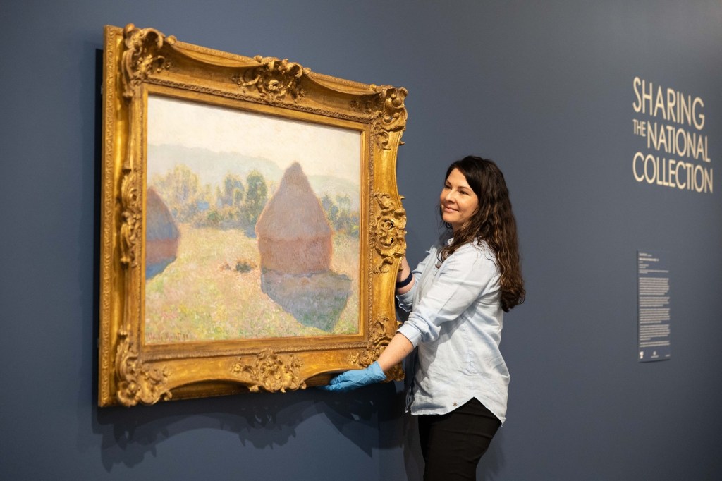 Gallery attendant holding painting by Claude Monet of a haystack.