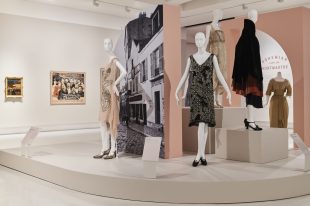 Installation view of a gallery showing mannequins in period Parisian dresses, there are also pictures on the wall. Paris: Impressions of Life.